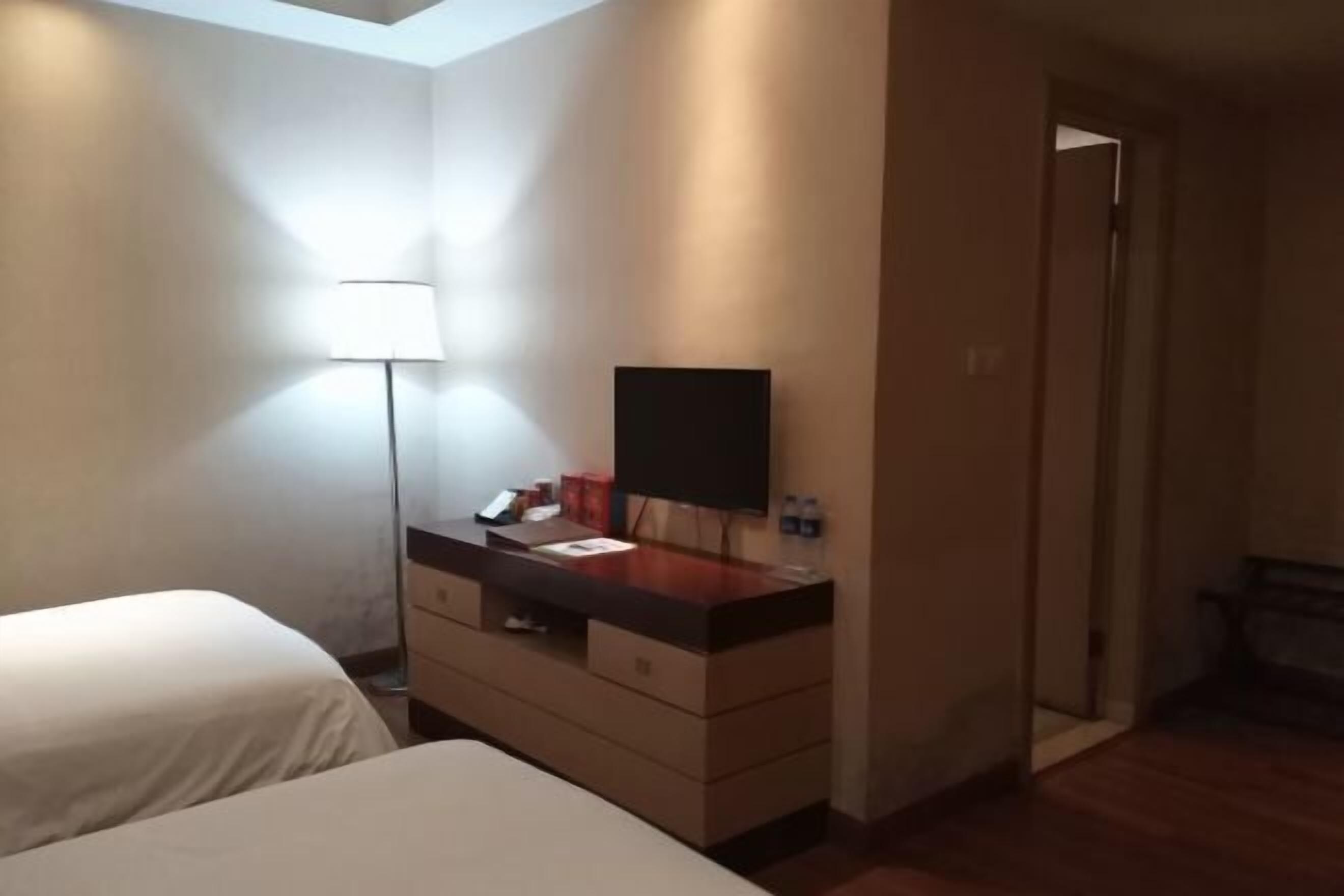 A hotel room with two beds, a dresser, a TV, and a lamp.
