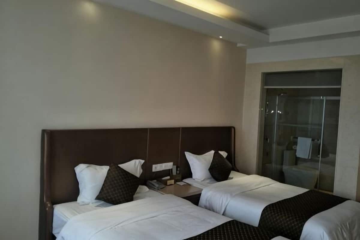 A hotel room with two beds, a nightstand, and a glass shower door.