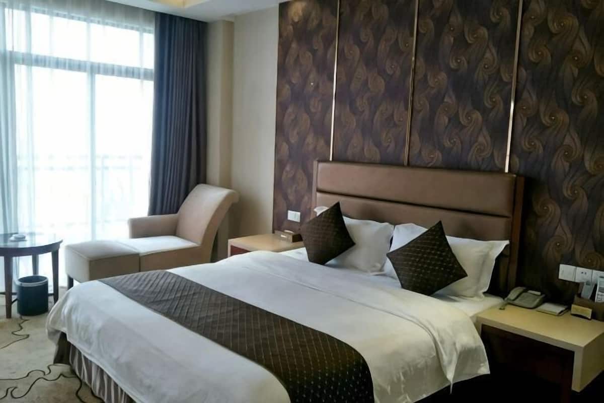 A hotel room with a large bed, a chair, a nightstand, and a view of the outdoors.