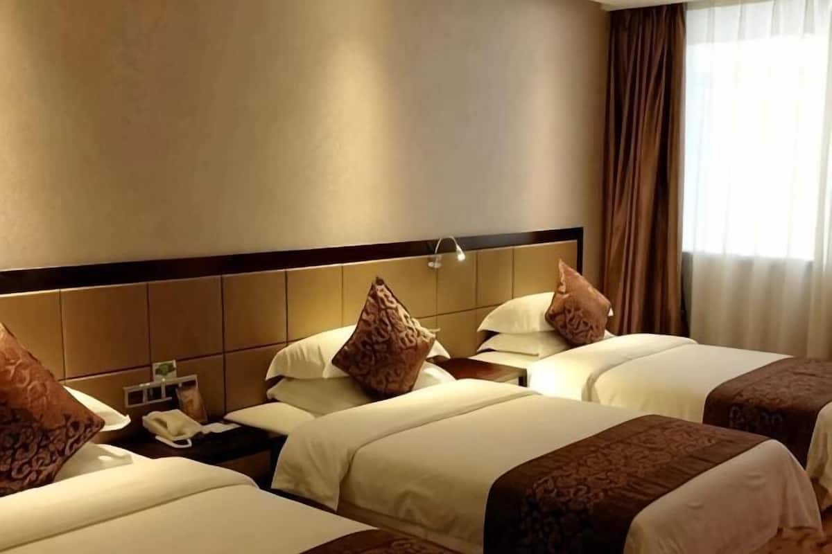 A hotel room with three beds, a headboard, a nightstand, and a window with curtains.