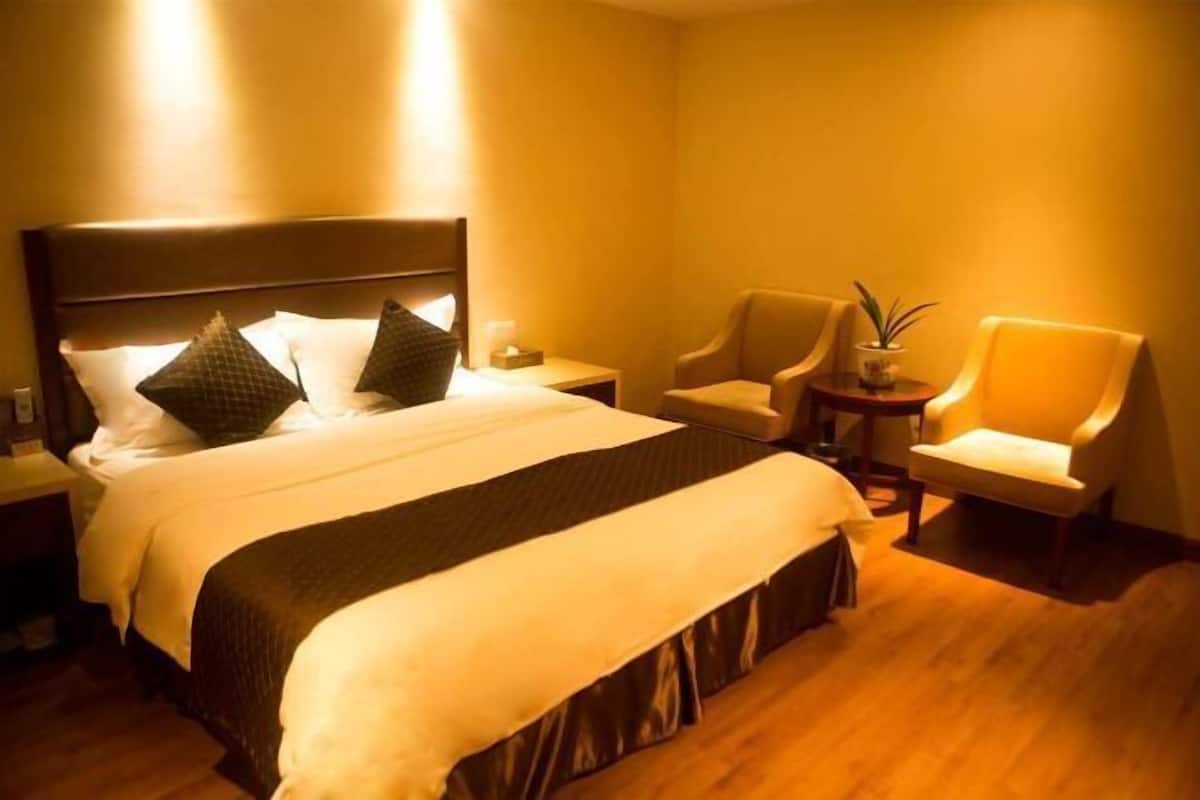 A hotel room with a large bed, two armchairs, a small table, and a potted plant.