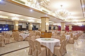 A banquet hall with round tables and chairs, chandeliers, and a stage area. - Joy Hotel (Fengkai)