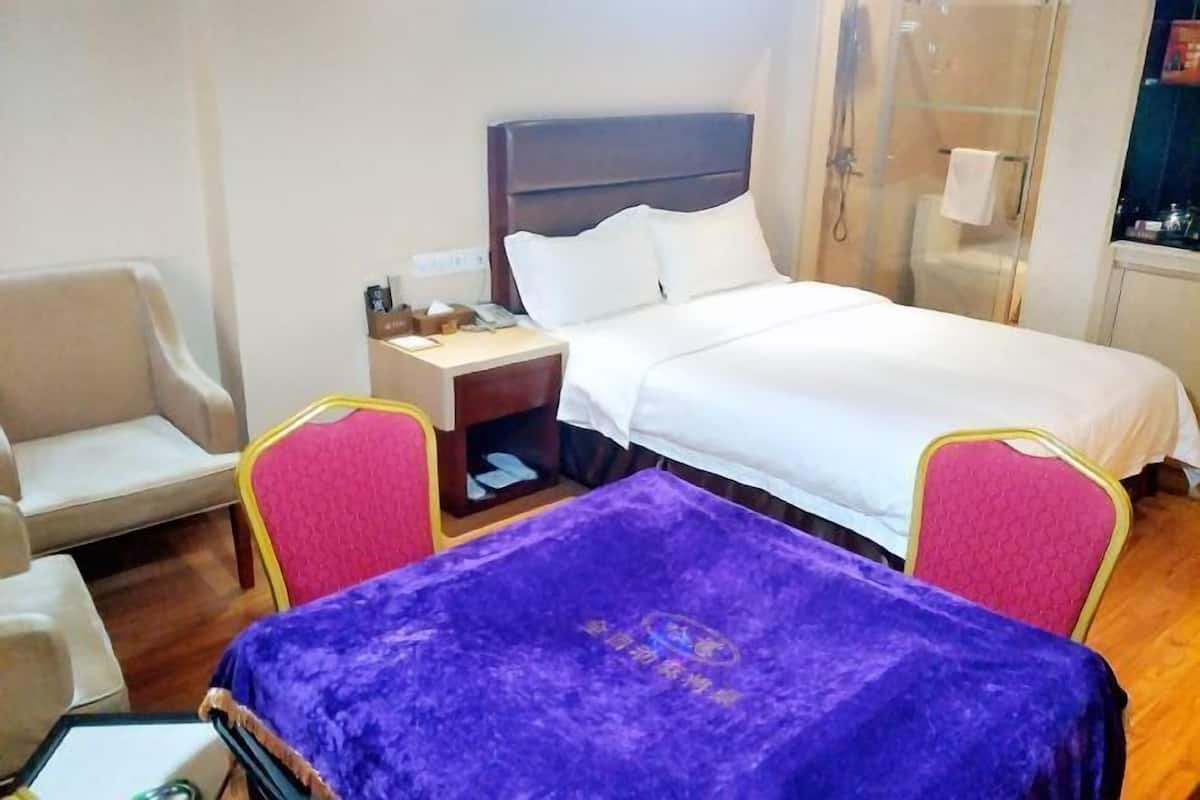 A hotel room with a bed, a nightstand, a desk with a purple cover, and a chair.