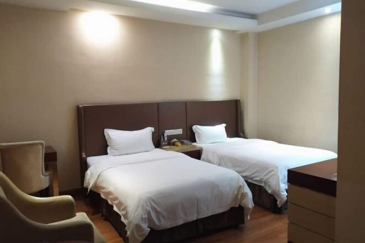 A hotel room with two single beds, a chair, a nightstand, and a dresser.