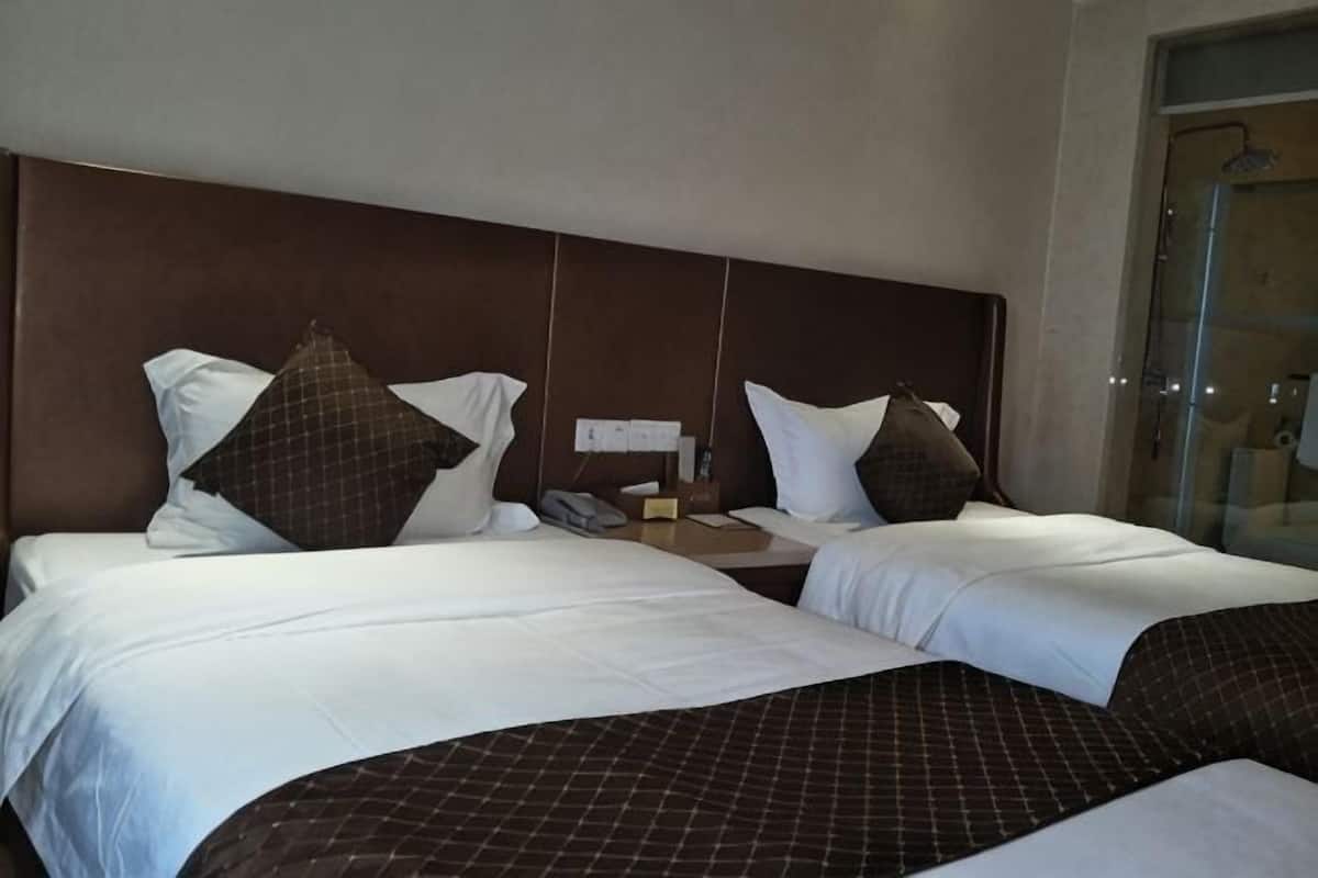 A hotel room with two beds, a wooden headboard, and a glass shower area.