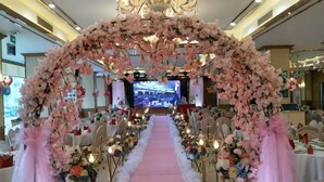 Un pasillo nupcial con decoración floral, sillas blancas y una alfombra rosa.