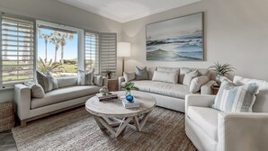 A living room with a sofa, armchairs, a coffee table, and a painting of the ocean.