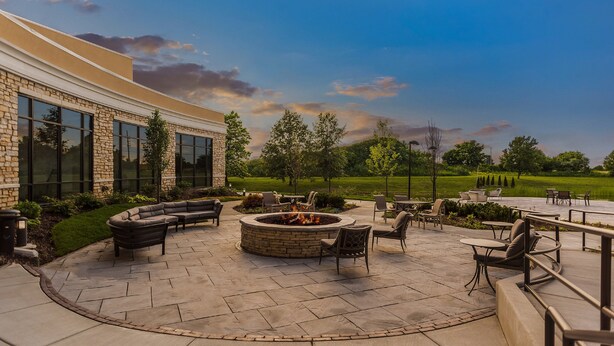 An outdoor patio area with a fire pit, seating, and a view of a building with large windows.