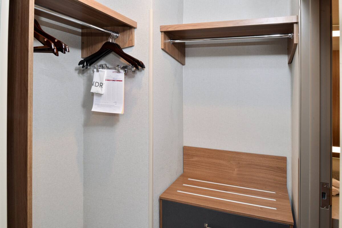 A walk-in closet with wooden shelves, a hanging rack, and a bench.