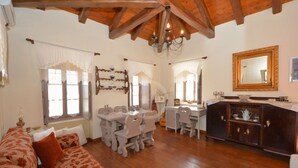 A cozy living room with a wooden ceiling, a dining area with a table and chairs, and a large mirror on the wall. - Estia Stone-Built Cottage, the perfect family getaway (Argolida)
