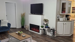 A living room with a fireplace, a television, a couch, and a kitchen area with cabinets and a countertop. - Blue Ridge Cozy Cabin with Full Mountain View (Blue Ridge)