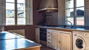Een keuken met witte kastjes, een fornuis, een wasmachine en een raam met uitzicht op buiten.