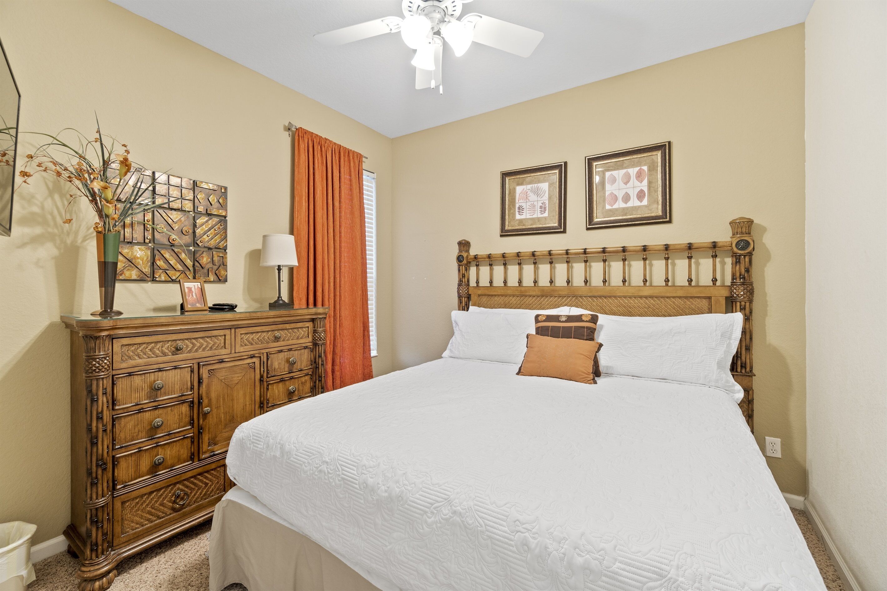 A bedroom with a wooden bed, a dresser, a ceiling fan, and two framed pictures on the wall.