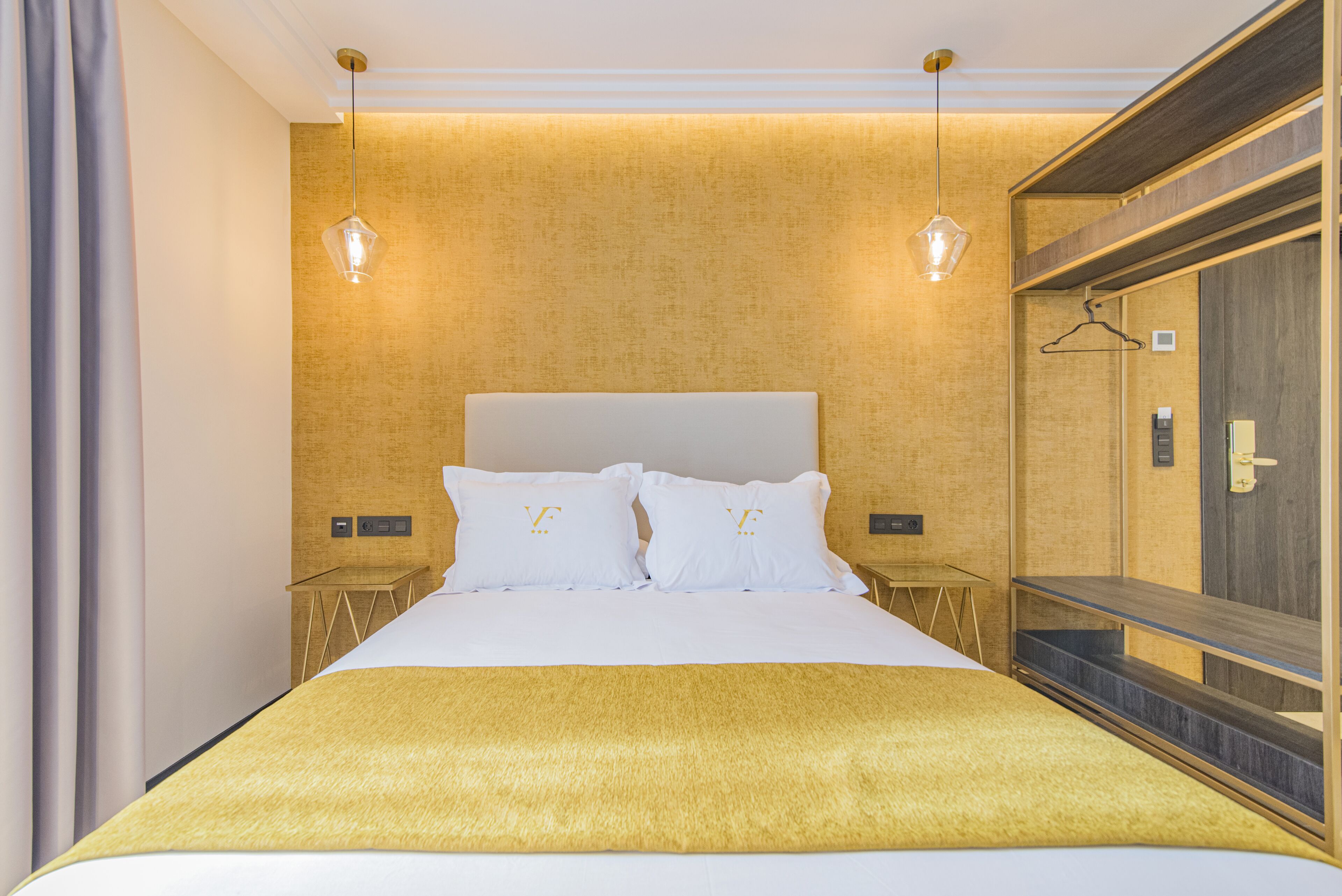 Una habitación de hotel con una cama grande, dos mesitas de noche, un espejo y una lámpara colgante.
