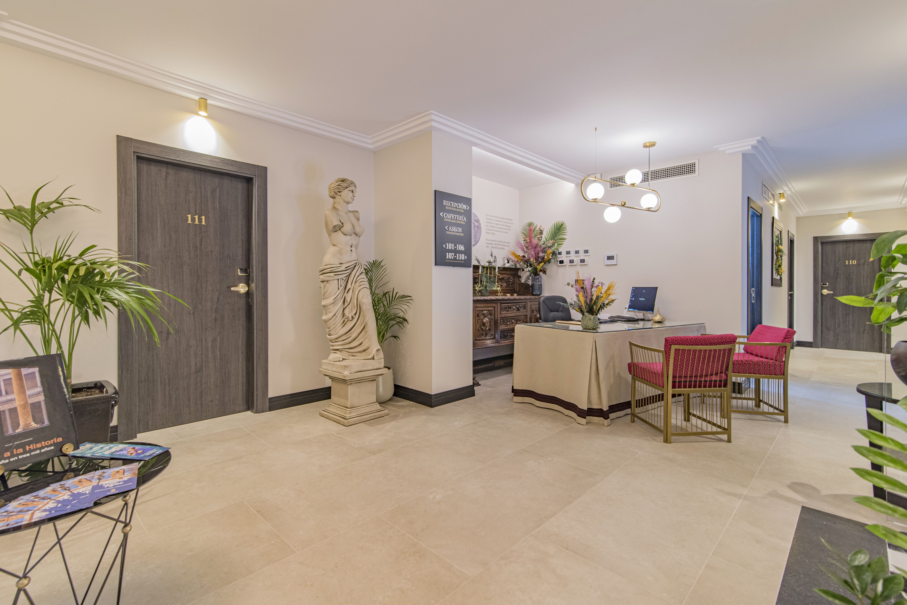 A reception area with a statue, a reception desk, and two red chairs.