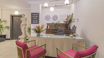 Un área de recepción con una estatua de mármol, un mostrador de recepción, dos sillas con cojines rosa y un aparador decorativo.