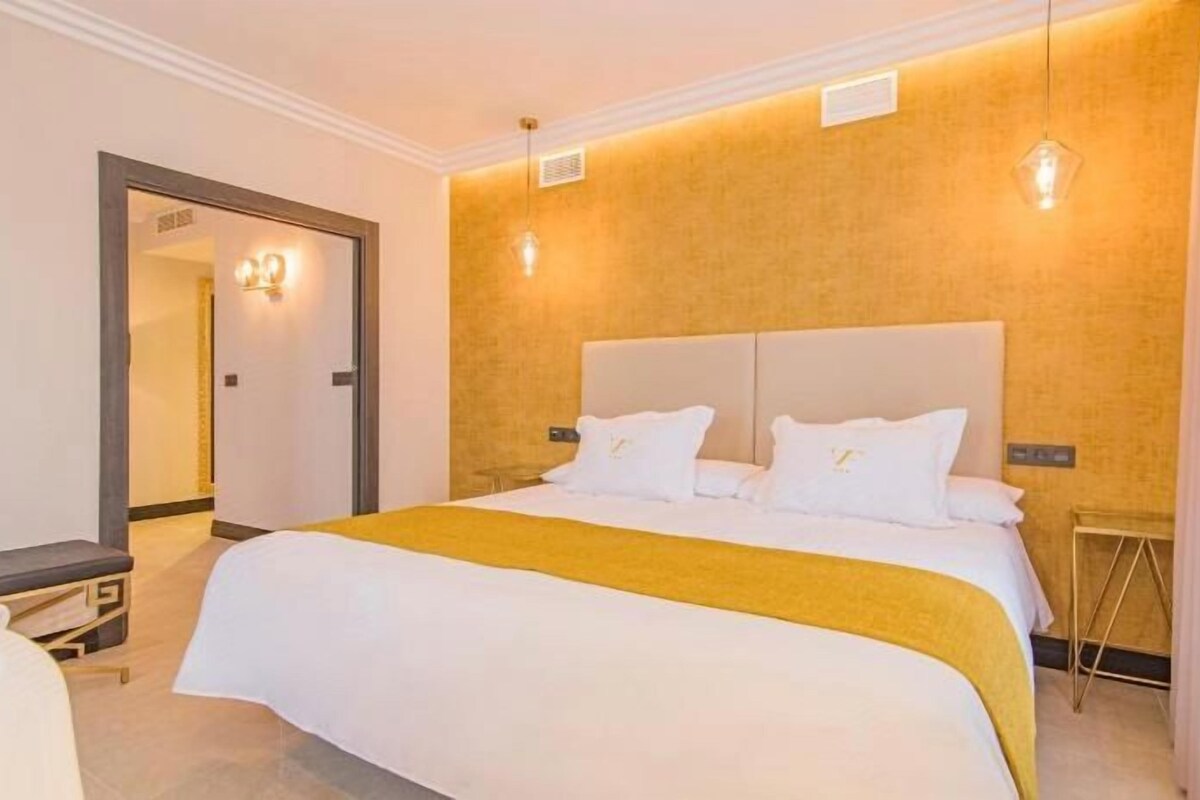 A hotel room with a large bed, a bedside table, a mirror, and a door leading to another room.