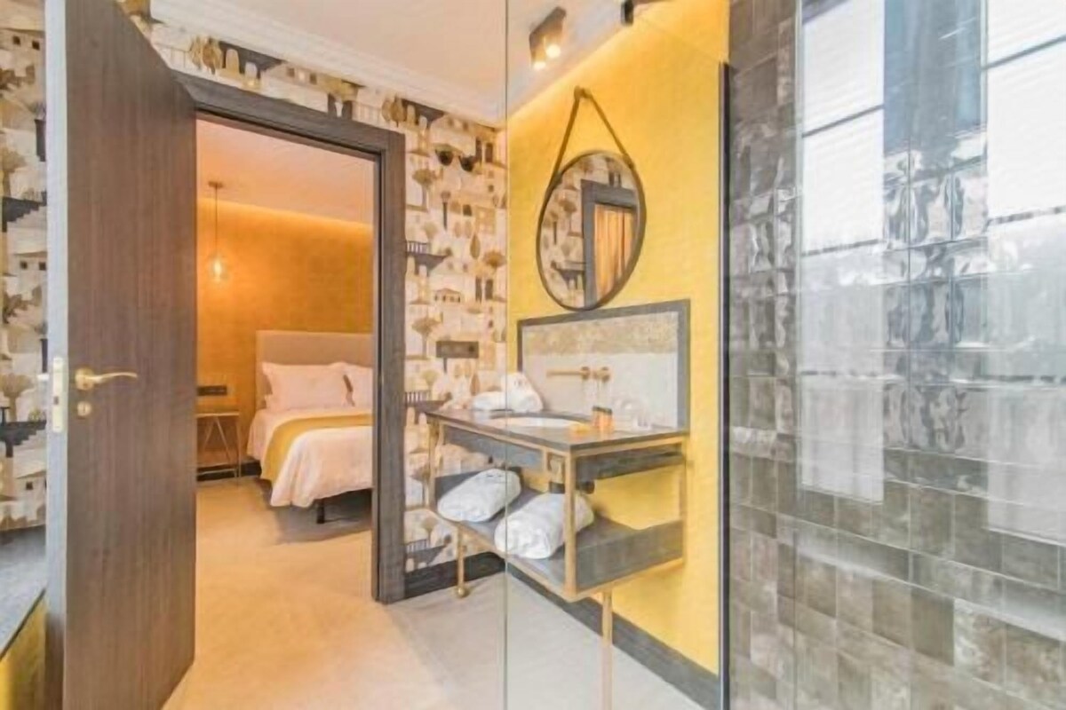 A hotel room with a bed, a bedside table, a mirror, and a bathroom with a sink and mirror.