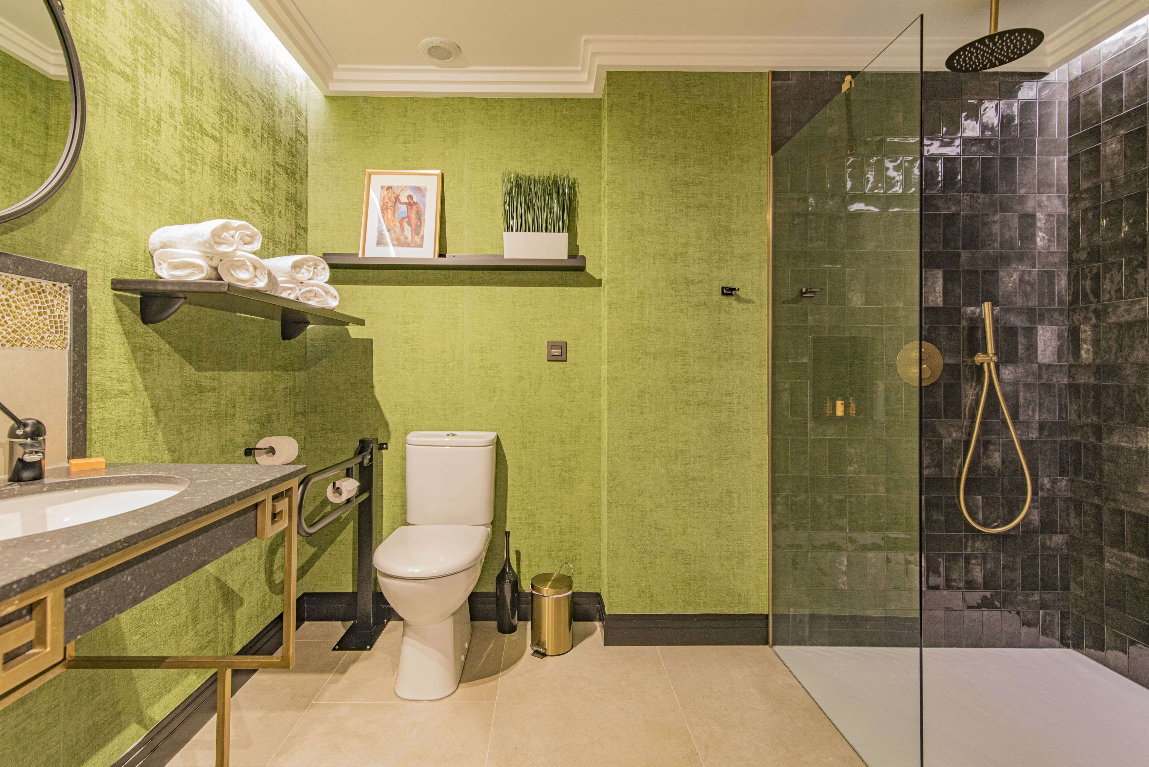 Een badkamer met een groene wand, een wit toilet, een douche met glazen deur en een wastafel met gouden lijst.