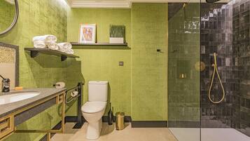 Een badkamer met een groene wand, een wit toilet, een douche met glazen deur en een wastafel met gouden lijst.