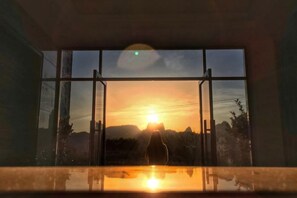 Una ventana con vista al atardecer y siluetas de árboles.