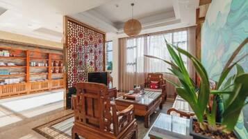 Un intérieur traditionnel avec une bibliothèque en bois, un élément de séparation décoratif, un coin repas comprenant une table et des chaises, et une grande plante en pot.