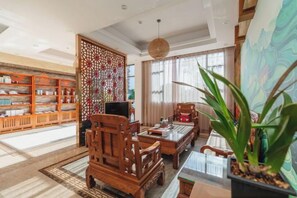 Un intérieur traditionnel avec une bibliothèque en bois, un élément de séparation décoratif, un coin repas comprenant une table et des chaises, et une grande plante en pot.