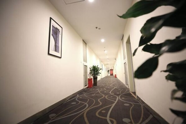 A hotel hallway with a patterned carpet, framed artwork on the walls, and potted plants. - 7Days Inn Chain Hotel (Chongqing Fuling Nanmenshan Pedestrian Street) (Chongqing)