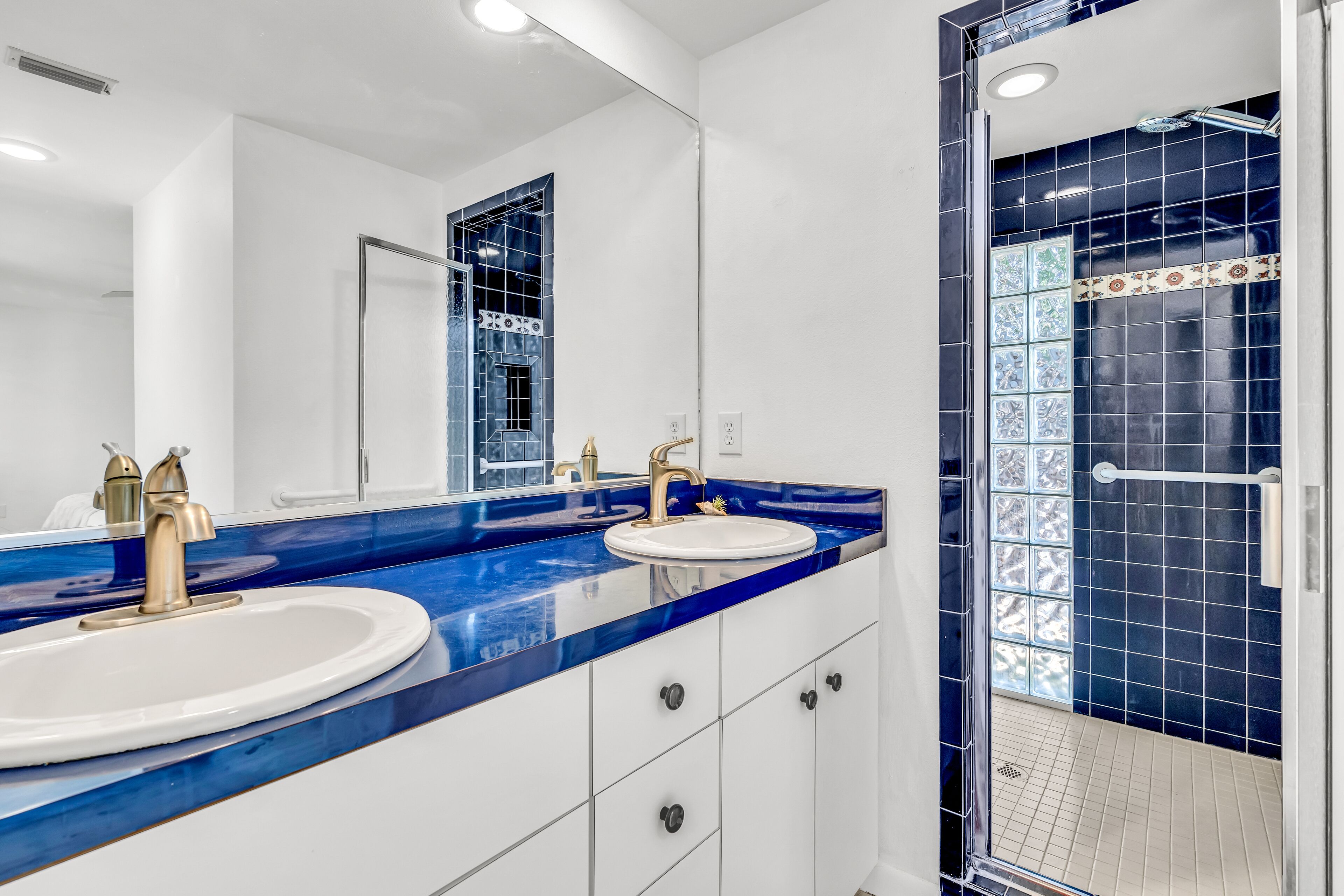 A modern bathroom with two sinks, a large mirror, and a shower area with blue tiles.