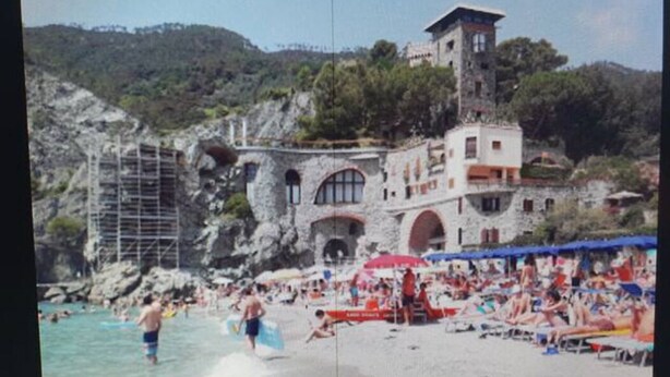 A beach with people, a building with arches, and a tower. - Casa Isabella Monterosso (Monterosso al Mare)