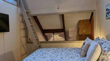Ein Schlafzimmer mit Bett, Holzboden, Deckenventilator, Fenster und einer Treppe.