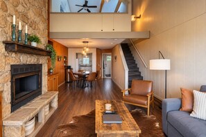 Una sala de estar moderna con chimenea de piedra, zona de comedor y escalera que lleva a un nivel superior.