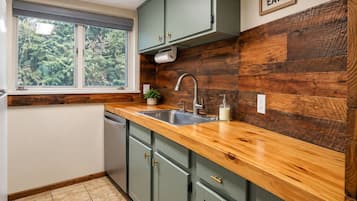A kitchen with a wooden countertop, a sink, and a window with a view of greenery.