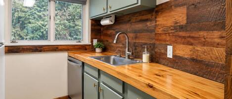 Una cocina con encimera de madera, un lavamanos y una ventana con vistas al verdor.