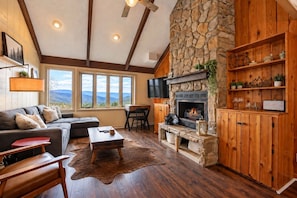 A cozy living room with a stone fireplace, wooden shelves, a sofa, and a view of the mountains. - The Beech Club *Mountain Views*Pet Friendly* (Beech Mountain)