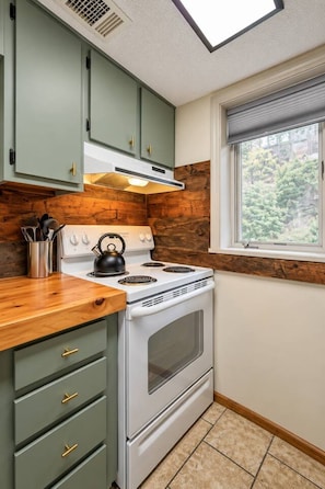 Una cocina con estufa, horno y ventana con vista a árboles.