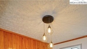 Een eetruimte met houten lambrisering, een ronde tafel, vier stoelen en een plafondlamp.