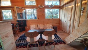 A wooden cabin bedroom with a bed, two chairs, a TV, and large windows.