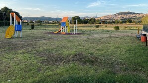 Une aire de jeux extérieure avec des toboggans et des structures d’escalade, située dans un champ herbeux, avec une vue sur la ville en arrière-plan.