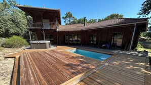 Una terraza de madera con piscina, jacuzzi y una zona de estar cubierta al aire libre.