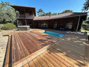 Una terraza de madera con piscina, jacuzzi y una zona de estar cubierta al aire libre.