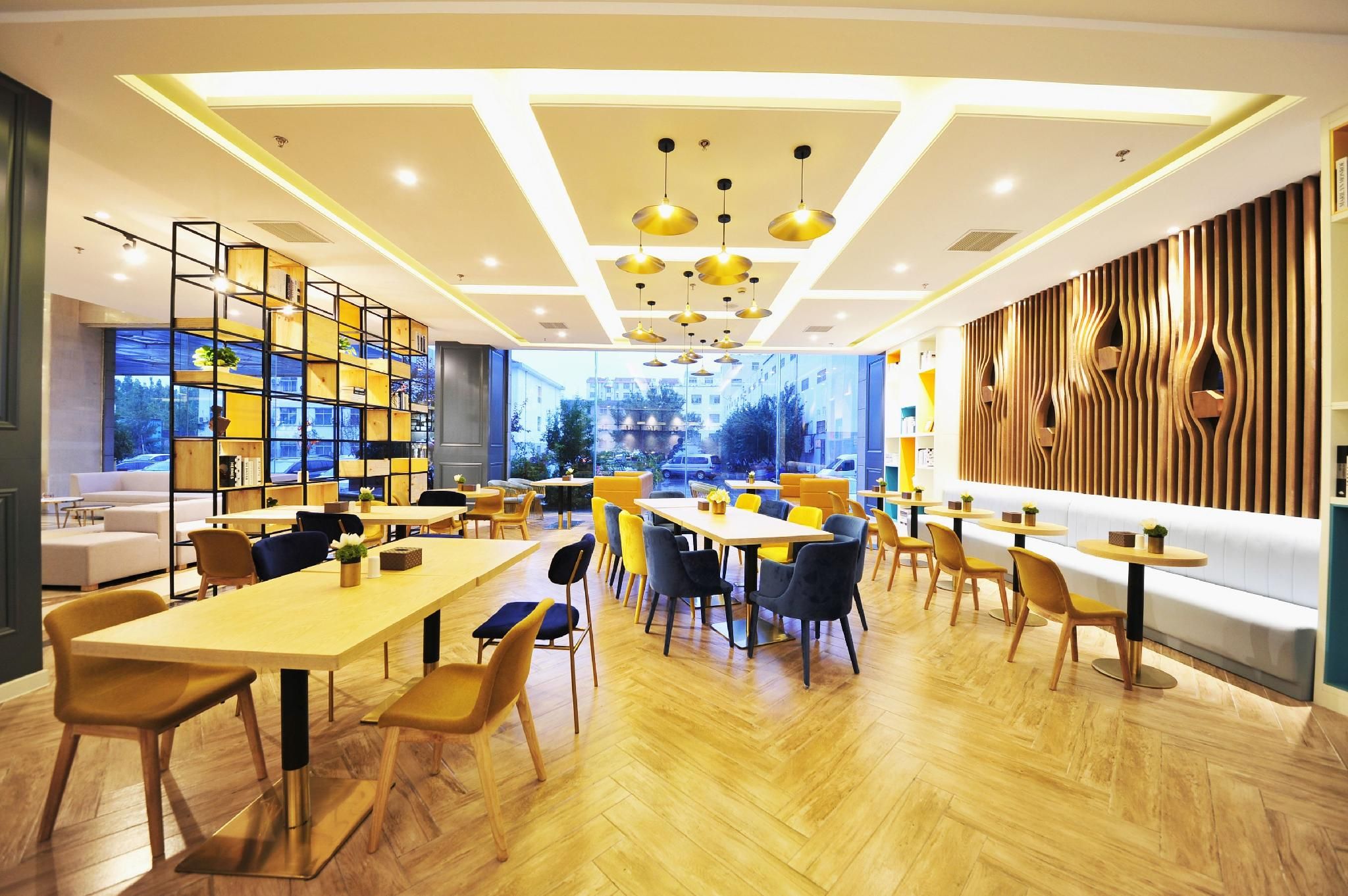 A modern dining area with wooden flooring, multiple tables and chairs, and a large window offering a view of the city.