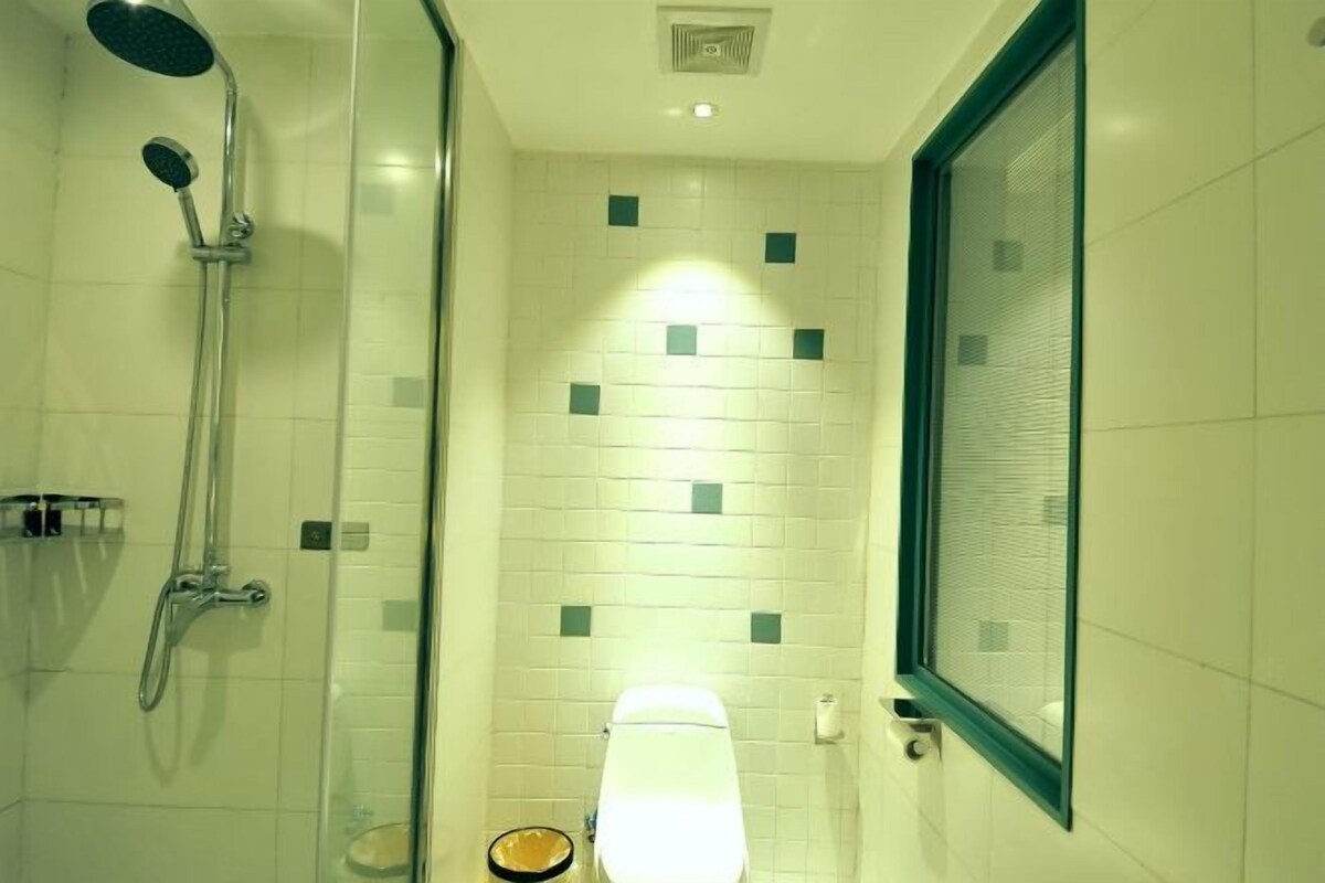 A bathroom with a glass shower enclosure, a toilet, and a window with a green frame.