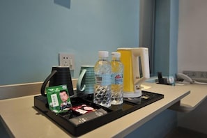 A hotel reception area with a counter, a green card, bottled water, a yellow box, and a coffee maker. - Magnotel (Rizhao)