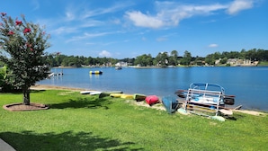 Vista para um lago com área gramada, um cais com barcos e uma árvore com flores cor-de-rosa.