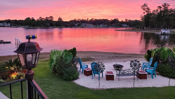 Um pátio à beira do lago com móveis de exterior e vista para o lago ao pôr do sol.