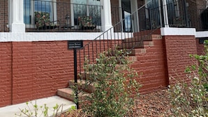 Uma casa de tijolos com varanda coberta, escadaria e um pequeno jardim.