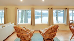 A room with a large window overlooking a lake, a white sofa, and two wicker chairs. - Falmouth Vacation Rental On Highland Lake! (Falmouth)