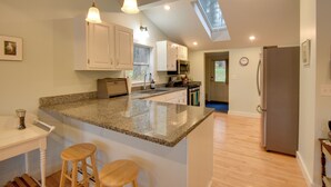 A kitchen with a large island, wooden stools, a refrigerator, and a skylight. - Falmouth Vacation Rental On Highland Lake! (Falmouth)