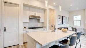 Une cuisine moderne avec des meubles blancs, un grand îlot central, des luminaires suspendus et un coin repas équipé de tabourets de bar.